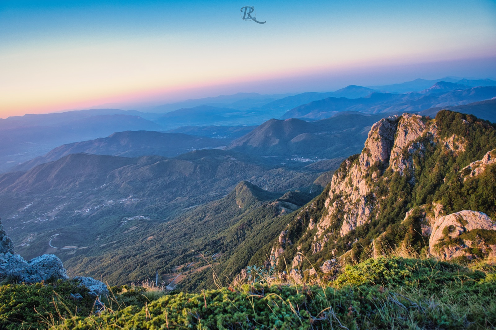 Creste rocciose in primo piano e catene di montagne in lontananza, nella luce calda del tramonto
