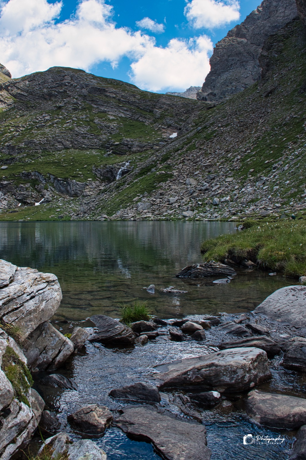 Rocce piatte sulla riva di un lago di montagna, con le cime e le nuvole sullo sfondo