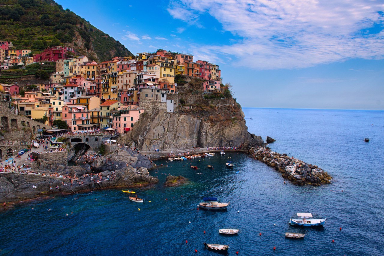 Case colorate arroccate su uno sperone di roccia sopra il mare, con piccole barche ancorate nella baia