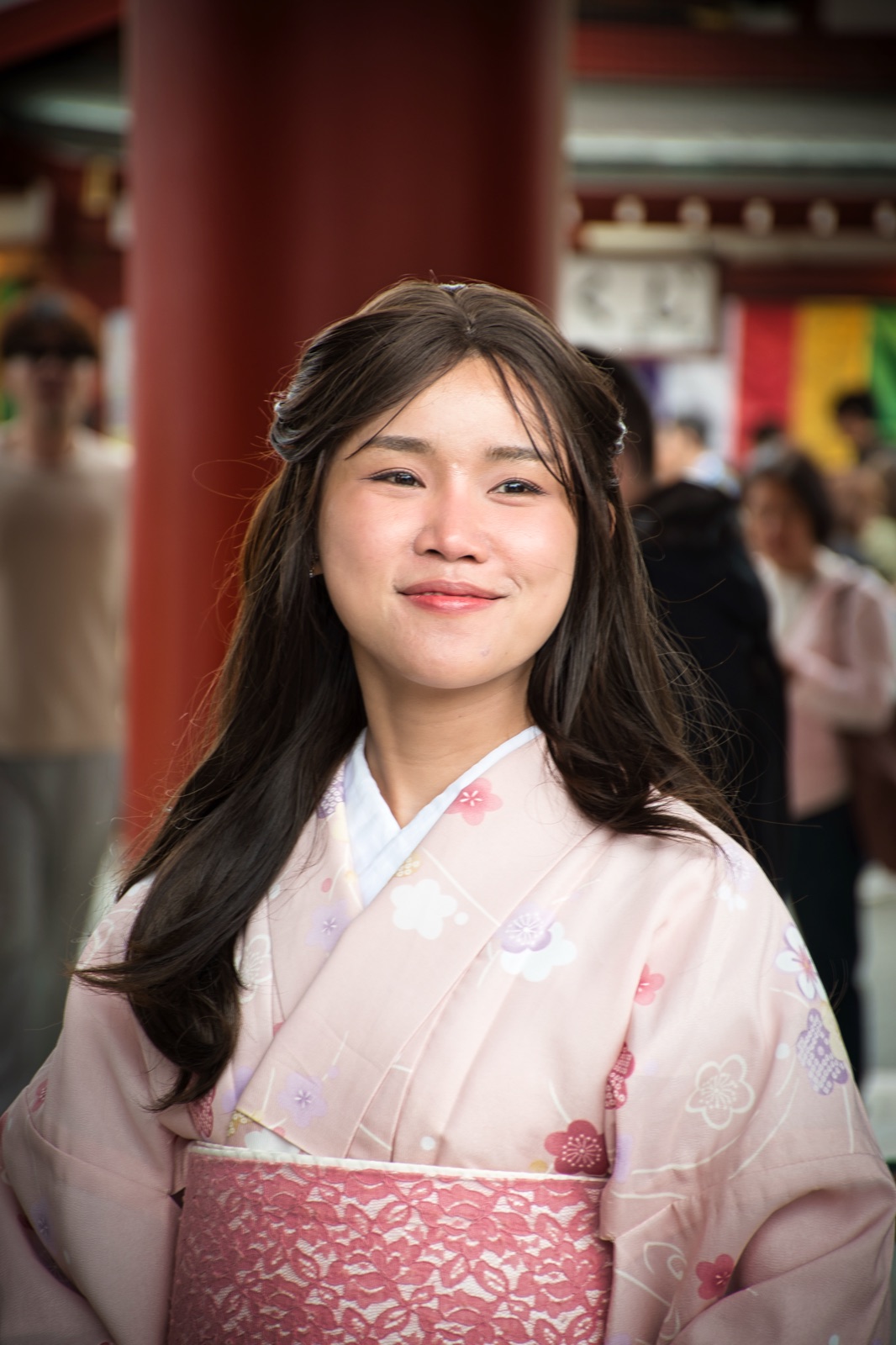 Ragazza dai lunghi capelli scuri in kimono rosa chiaro, davanti alla colonna rossa di un tempio