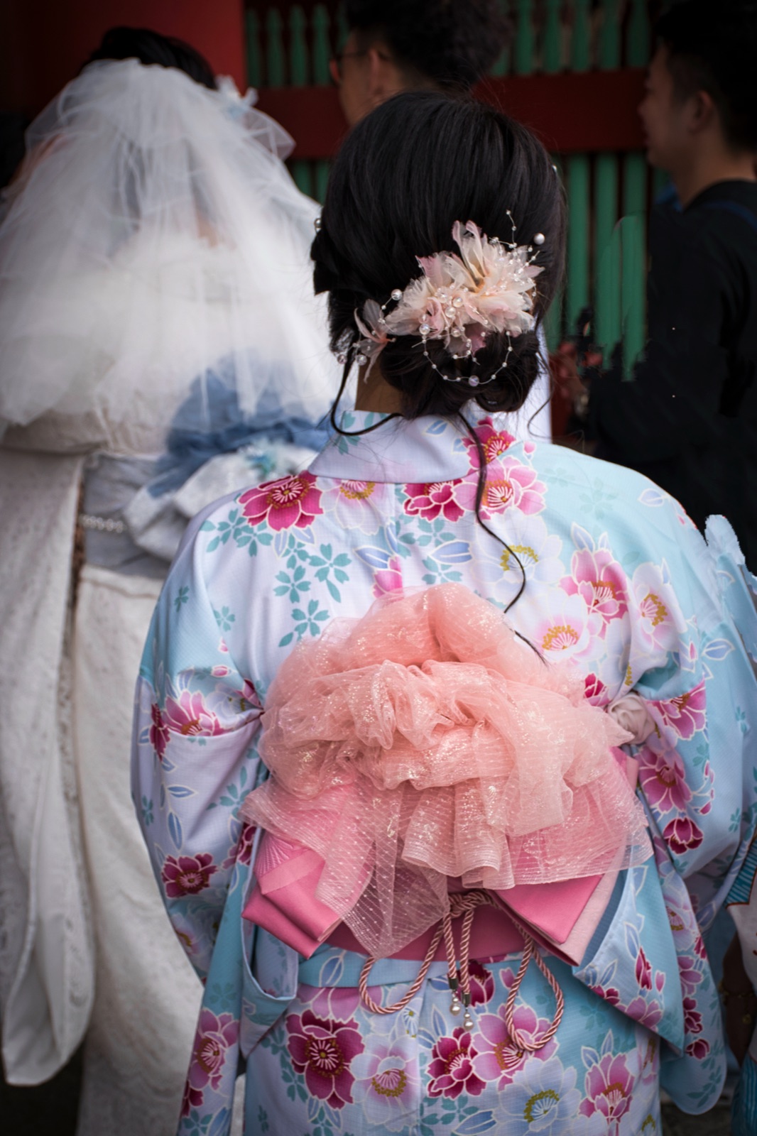 Ragazza vista di spalle in kimono azzurro a fiori, con un grande fiocco rosa sulla schiena e un fermaglio fiorito tra i capelli
