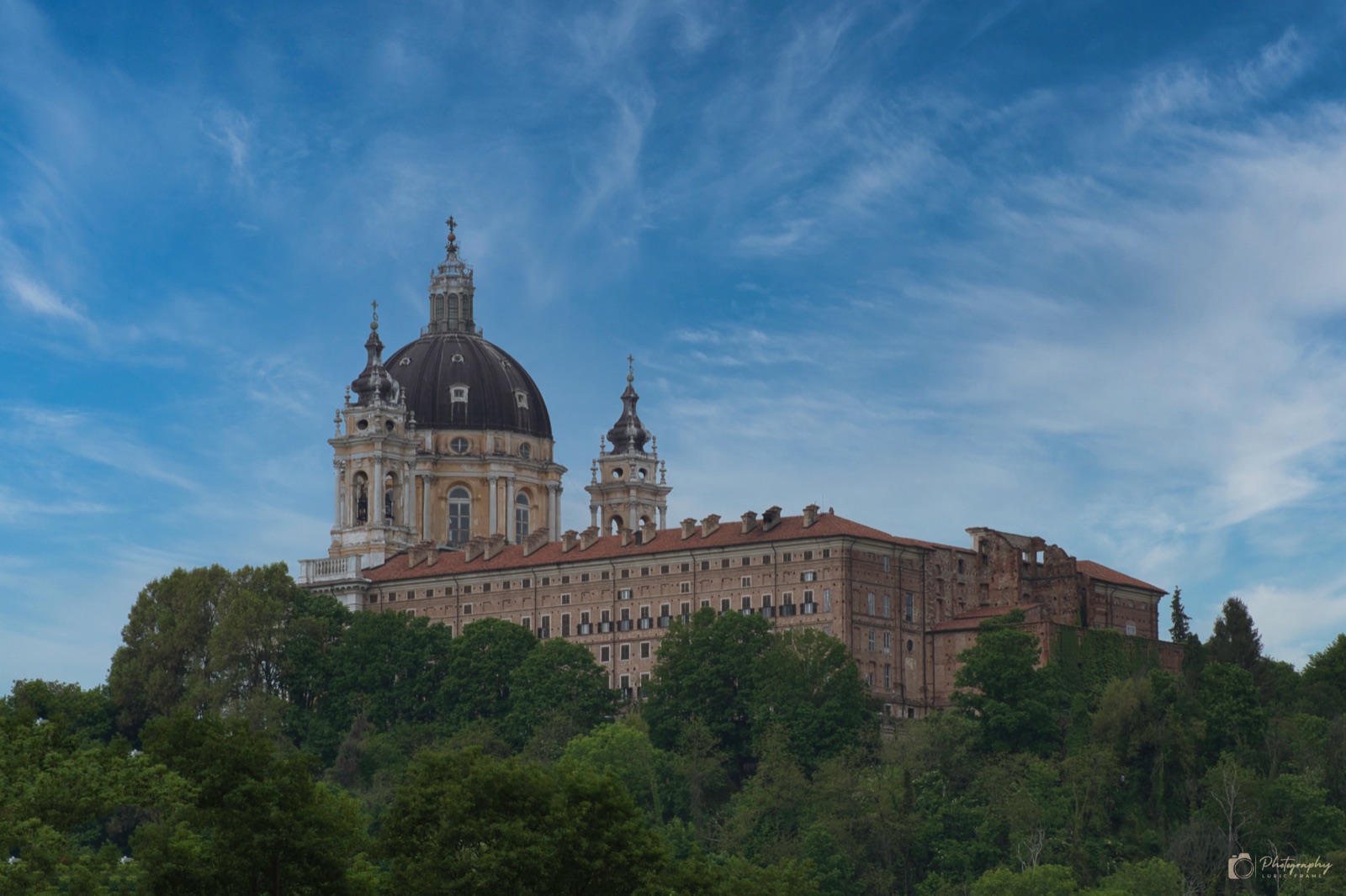 Grande basilica con cupola e due campanili sopra un bosco verde, sotto un cielo azzurro con nuvole